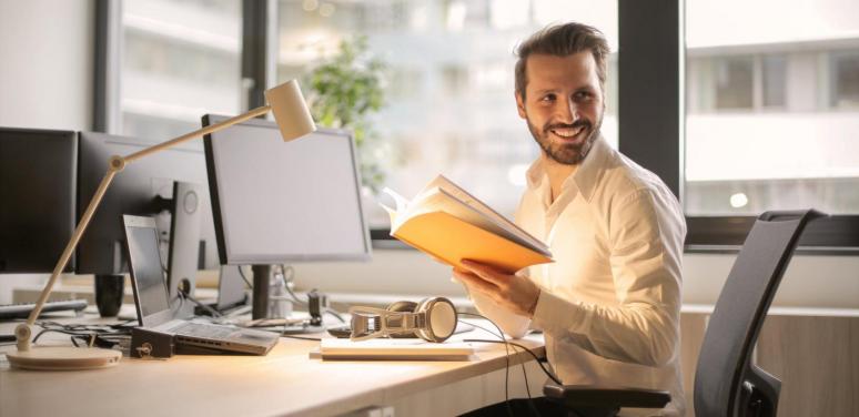 man sitting at a desk smiling turned to face someone off camera 